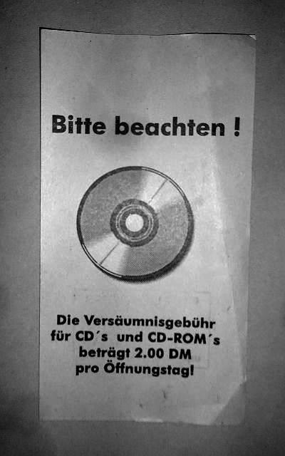 an old note from a library with a picture of a CD with german text “Please note! The missing fee for CD’s and CD-ROMs is 2.00 DM per opening day!”