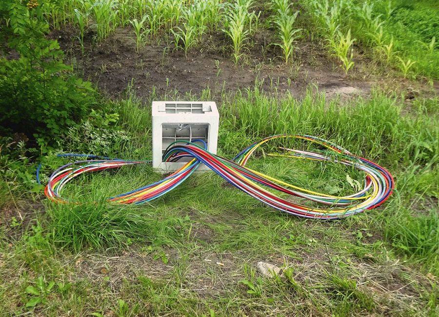 open power box between street and field, colorful fiber internet cables are twirling out of it in a loop