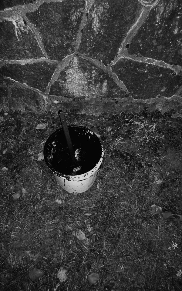 lost bucket of black paint next to a stone wall