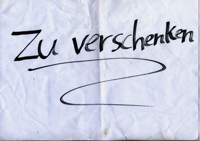 piece of paper with handwritten words “Zu Verschenken” (Give Away), and a swoosh underline